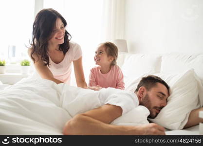 people, family and morning concept - happy child with parents waking up in bed at home