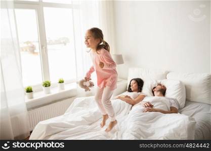 people, family and morning concept - happy child with toy and parents in bed at home