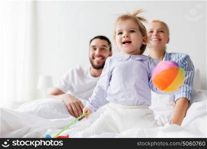 people, family and morning concept - happy child with toys and parents in bed at home. happy child with toys and parents in bed at home