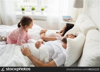 people, family and morning concept - happy little girl waking her sleeping parents up in bed at home