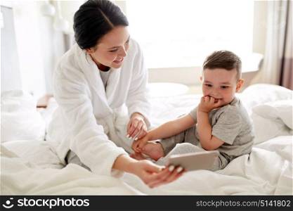 people, family and morning concept - happy mother and little son with smartphone in bed at home or hotel room. mother and son with smartphone in bed at hotel