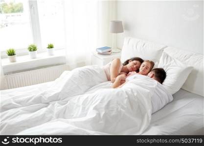 people, family and rest concept - happy child with parents sleeping in bed at home. happy family sleeping in bed at home