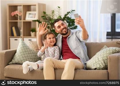 people, family and technology concept - happy father and little daughter taking selfie by smartphone sitting on sofa at home. father and daughter taking selfie at home