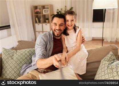 people, family and technology concept - happy father and little daughter taking picture by selfie stick at home. father and daughter taking selfie at home