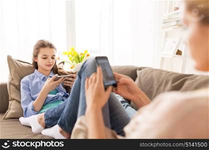 people, family and technology concept - happy girl and mother with smartphones at home. happy family with smartphones at home