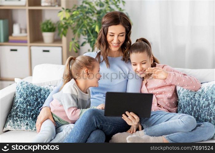 people, family and technology concept - happy mother and two daughters with tablet pc computer having video call at home. mother and children having video call on tablet pc