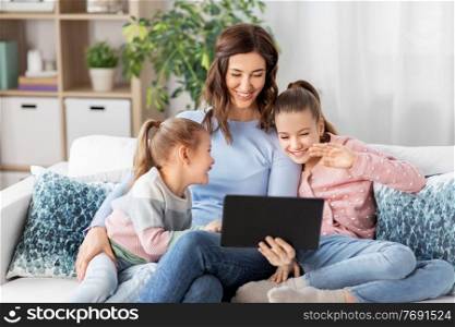 people, family and technology concept - happy mother and two daughters with tablet pc computer having video call at home. mother and children having video call on tablet pc
