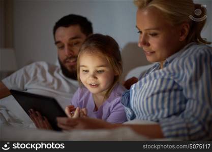 people, family and technology concept - happy mother, father and little girl with tablet pc computer in bed at night home. happy family with tablet pc in bed at home