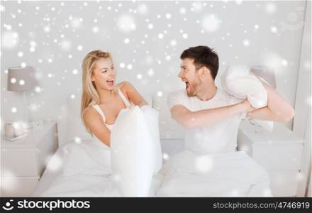 people, family, bedtime and fun concept - happy couple having pillow fight in bed at home over snow