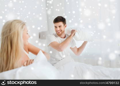 people, family, bedtime and fun concept - happy couple having pillow fight in bed at home over snow