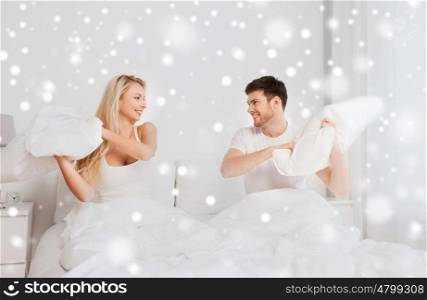people, family, bedtime and fun concept - happy couple having pillow fight in bed at home over snow