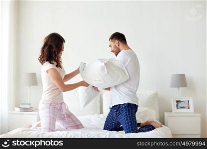 people, family, bedtime and fun concept - happy couple having pillow fight in bed at home. happy couple having pillow fight in bed at home
