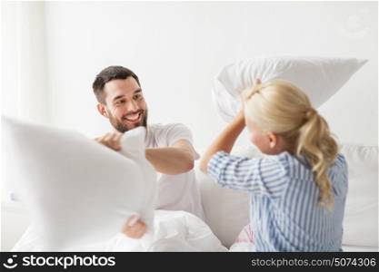 people, family, bedtime and fun concept - happy couple having pillow fight in bed at home. happy couple having pillow fight in bed at home