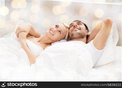 people, family, bedtime and happiness concept - happy couple lying in bed at home over lights background