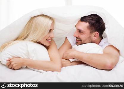 people, family, bedtime and happiness concept - happy couple lying in bed covered with blanket over head and talking at home