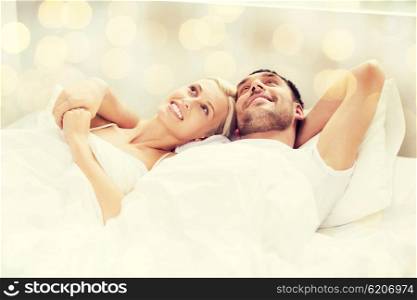 people, family, bedtime and happiness concept - happy couple lying in bed at home over lights background