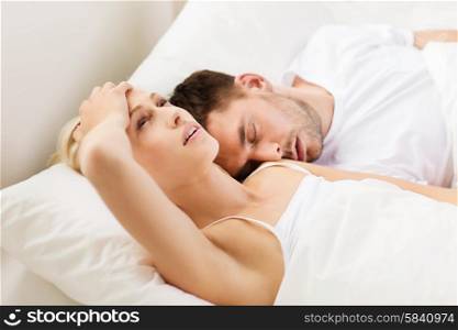 people, family, bedtime and insomnia concept - unhappy woman having sleepless night with sleeping and snoring man in bed at home
