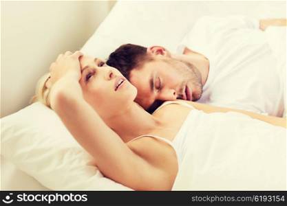 people, family, bedtime and insomnia concept - unhappy woman having sleepless night with sleeping and snoring man in bed at home