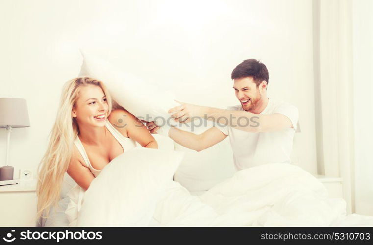 people, family, fun, bedtime and fun concept - happy couple having pillow fight in bed at home. happy couple having pillow fight in bed at home