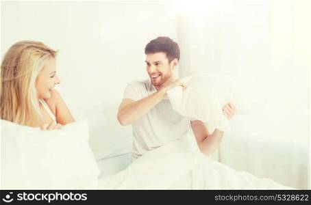 people, family, fun, bedtime and fun concept - happy couple having pillow fight in bed at home. happy couple having pillow fight in bed at home