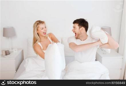 people, family, fun, bedtime and fun concept - happy couple having pillow fight in bed at home
