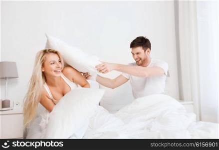 people, family, fun, bedtime and fun concept - happy couple having pillow fight in bed at home