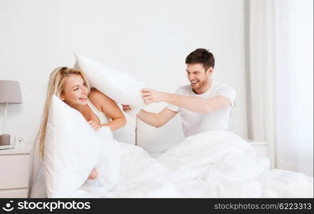 people, family, fun, bedtime and fun concept - happy couple having pillow fight in bed at home