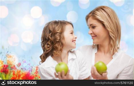 people, family, healthy eating and parenting concept - happy mother and daughter with green apples over poppy field background
