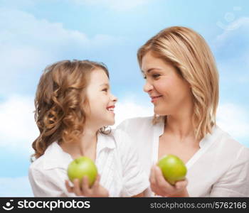 people, family, healthy eating and parenting concept - happy mother and daughter with green apples over blue sky background