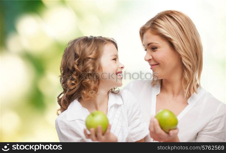 people, family, healthy eating and parenting concept - happy mother and daughter with apples over green background