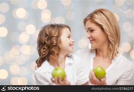 people, family, healthy eating and parenting concept - happy mother and daughter with green apples over lights background