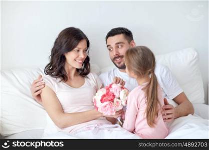 people, family, holidays and morning concept - happy little girl giving flowers to mother in bed at home
