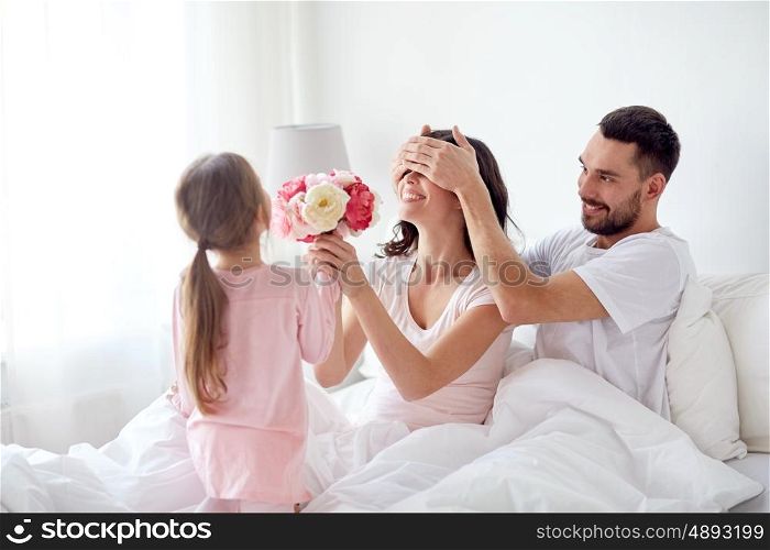 people, family, holidays and morning concept - happy little girl giving flowers to mother in bed at home