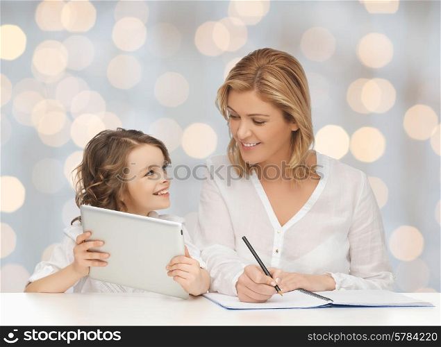 people, family, home education, children and technology concept - happy mother and daughter with tablet pc and notebook over holidays lights background
