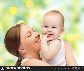 people, family, motherhood and children concept - happy mother hugging adorable baby with finger in his mouth over green lights background
