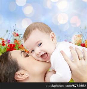 people, family, motherhood and children concept - happy mother hugging adorable baby over blue lights and poppy field background