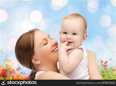 people, family, motherhood and children concept - happy mother hugging adorable baby with finger in his mouth over blue lights and poppy field background