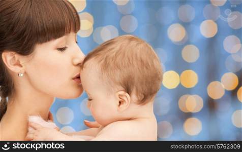 people, family, motherhood and children concept - happy mother hugging adorable baby over blue lights background