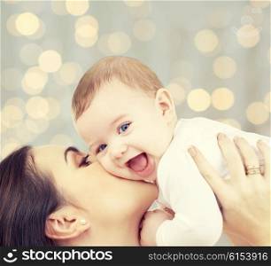 people, family, motherhood and children concept - happy mother hugging adorable baby over holidays lights background