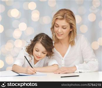 people, family, school, home education and parenting concept -happy mother and daughter doing homework and writing in notebook over holidays lights background