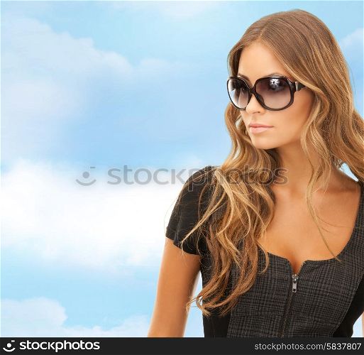 people, fashion, elegance and style concept - beautiful young woman in shades over blue sky and cloud background