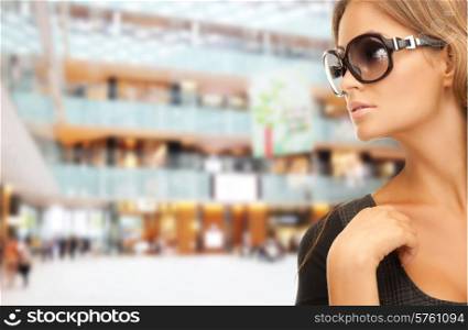 people, fashion, shopping, eyewear and style concept - beautiful woman in shades over mall background