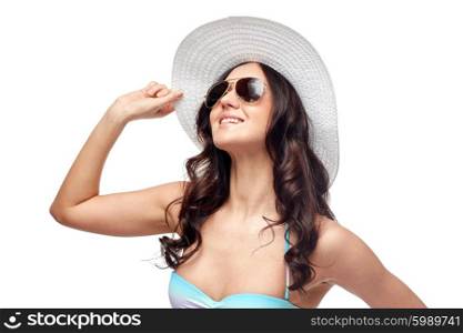 people, fashion, summer and beach concept - happy young woman in bikini swimsuit, sunglasses and sun hat