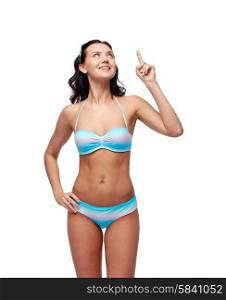 people, fashion, swimwear, summer and beach concept - happy young woman in bikini swimsuit pointing finger and looking up to something imaginary