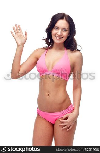 people, fashion, swimwear, summer and beach concept - happy young woman in pink bikini swimsuit waving hand