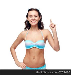 people, fashion, swimwear, summer and beach concept - happy young woman in bikini swimsuit pointing finger up to something imaginary
