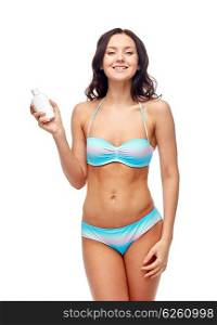 people, fashion, swimwear, summer and beach concept - happy young woman in bikini swimsuit holding sunscreen bottle
