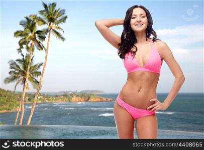 people, fashion, swimwear, summer and travel concept - happy young woman posing in pink bikini swimsuit over Sri Lanka beach with palms swimming pool background