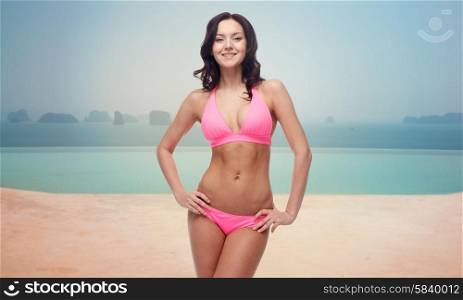 people, fashion, swimwear, summer and travel concept - happy young woman posing in pink bikini swimsuit over resort swimming pool or beach