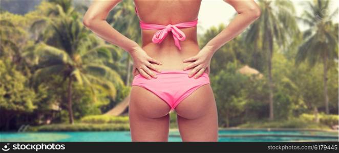 people, fashion, swimwear, summer beach and beauty concept - close up of young woman buttocks in pink bikini over swimming pools and palm trees background
